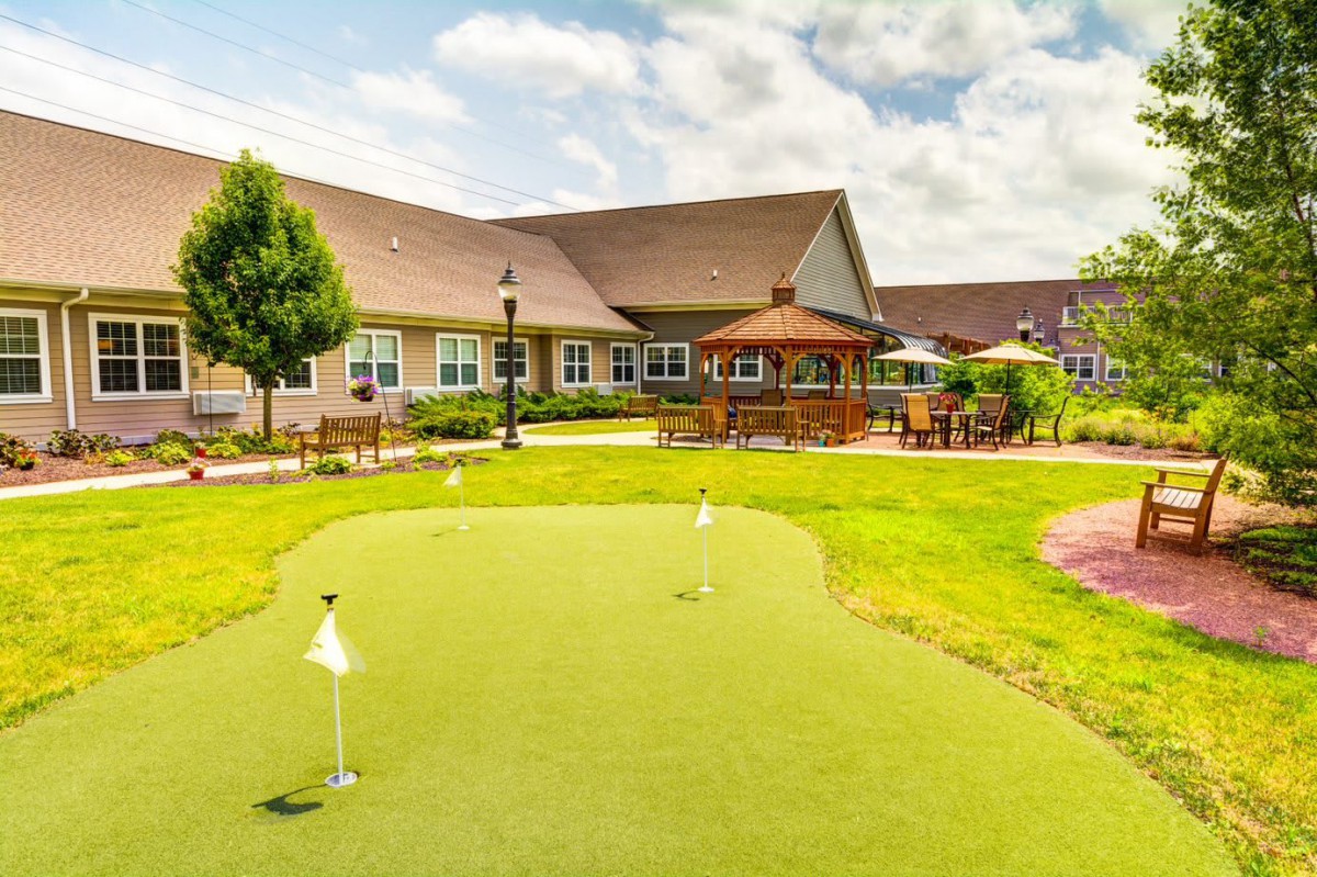 A scenic view of a putting green in front of a residential building, surrounded by well-maintained gardens and outdoor seating areas.