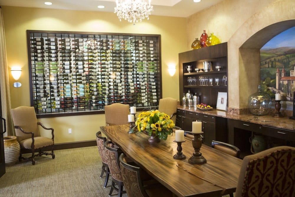 A stylish dining room featuring a large wine display, elegant chandelier, and a wooden table adorned with decorative candles and flowers.