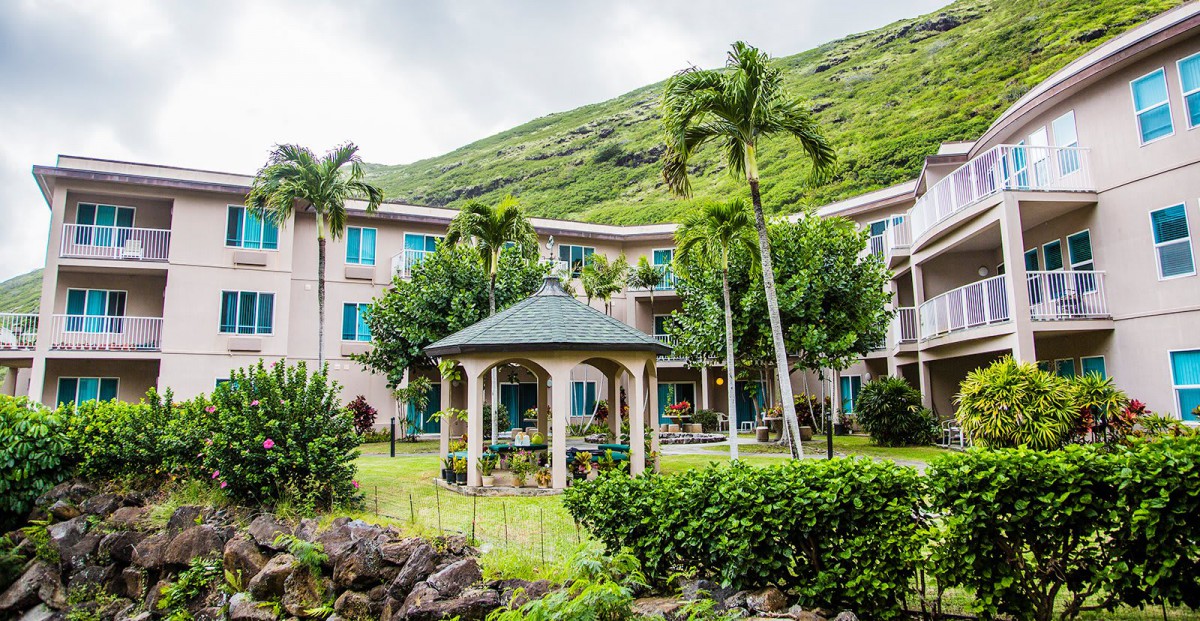 A tropical garden with a gazebo in front of a large building, surrounded by lush greenery and mountains.