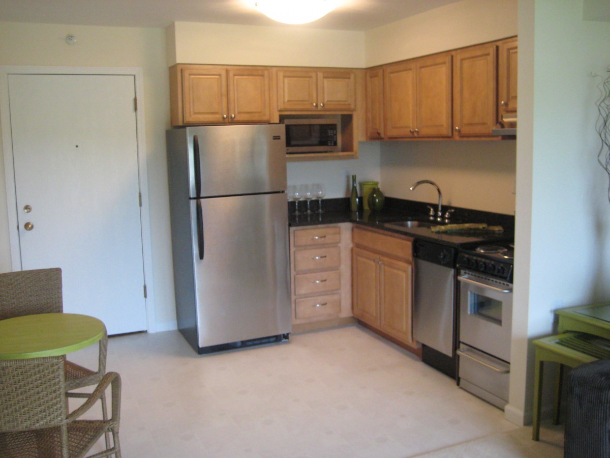 A modern, compact apartment kitchen with stainless steel appliances and wood cabinets.