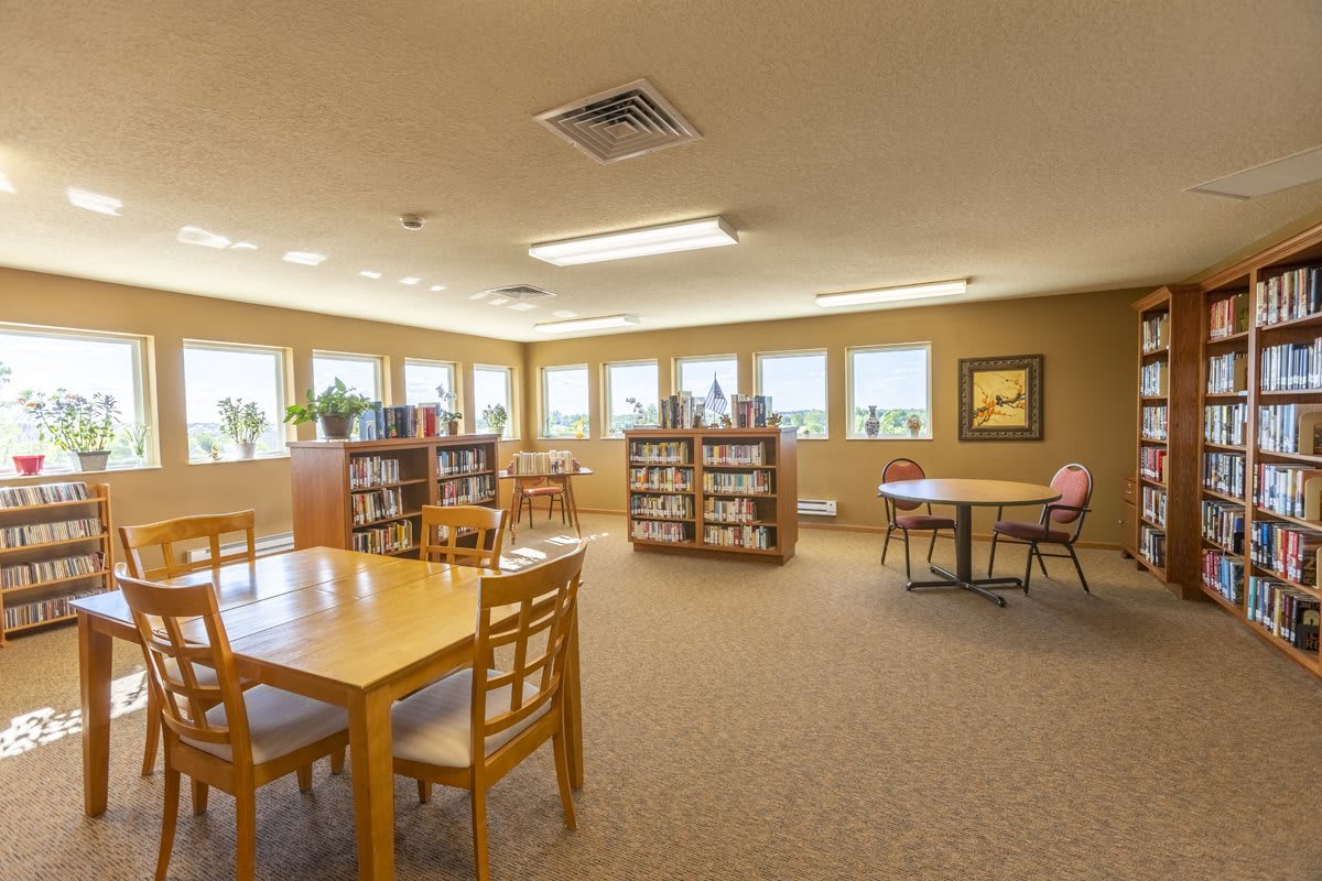 A cozy library space with bookshelves, tables, and chairs for reading.