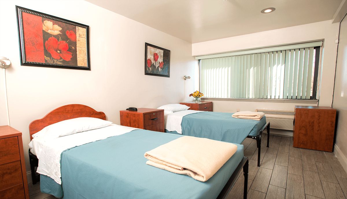 A simple hotel room with two single beds, decorated with light blue bedspreads and minimal artwork on the walls.