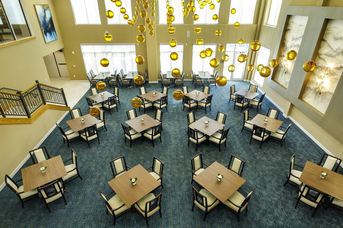 A modern dining area with several tables and chairs, featuring hanging lights and a carpeted floor.