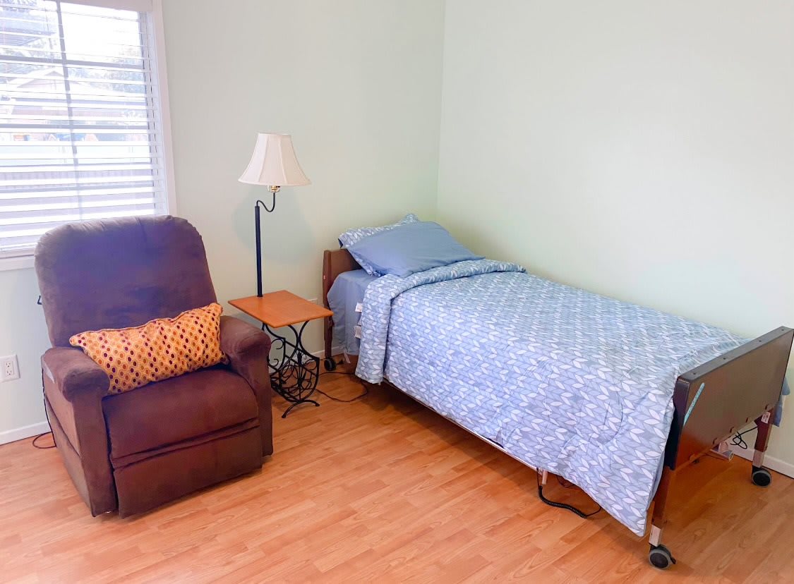 A simple bedroom with a single bed, recliner, and side table.
