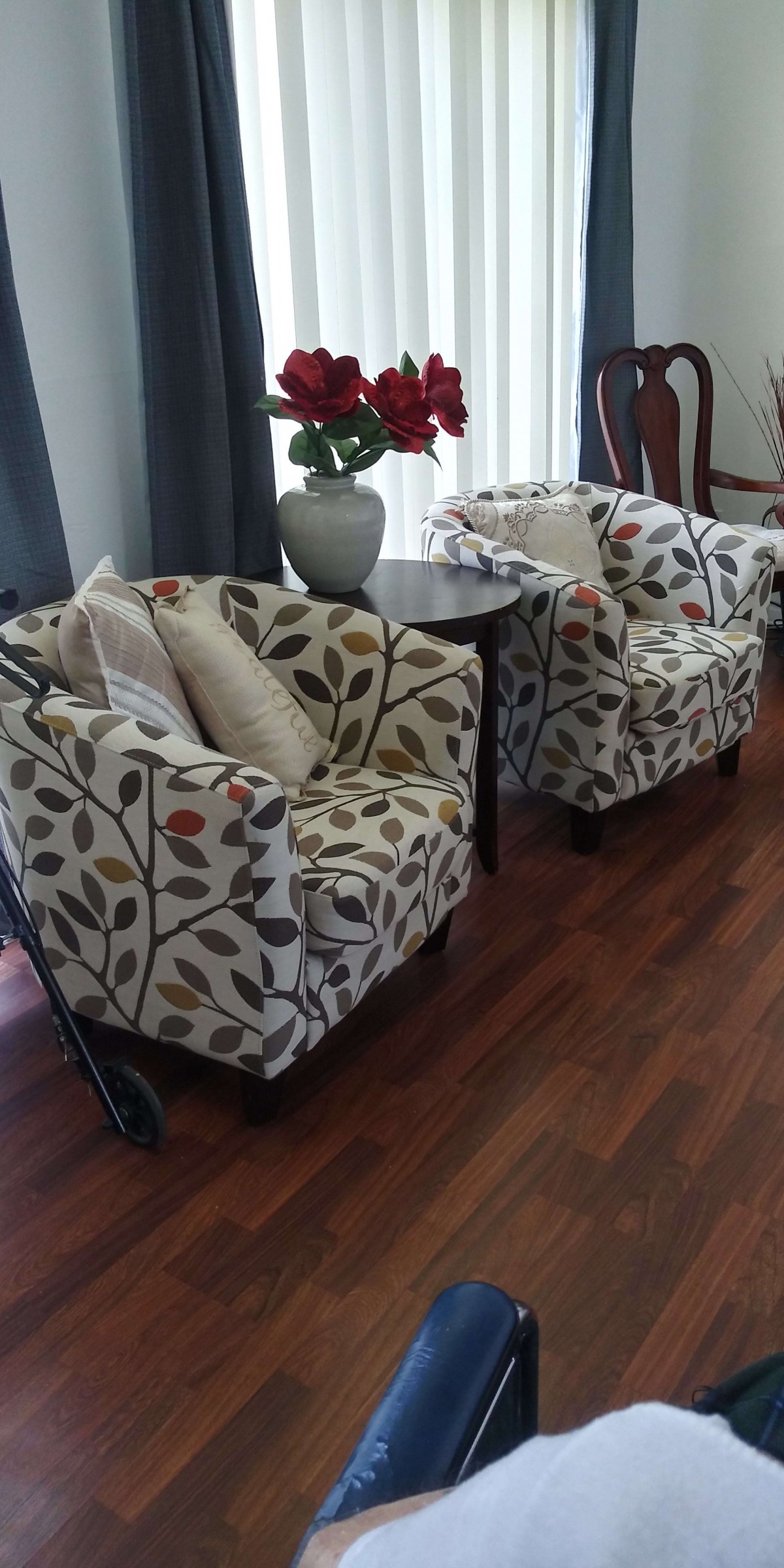 Two patterned armchairs with floral upholstery sit beside a small round table with a decorative vase on a wooden floor.