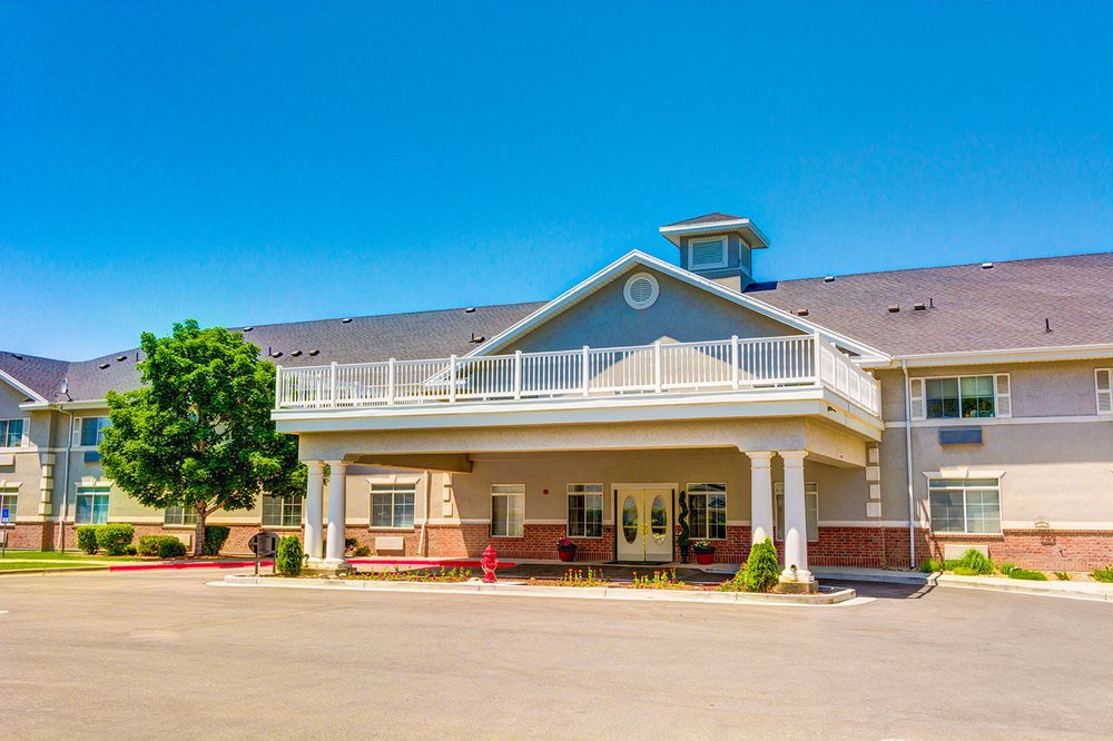 A sunny daytime view of a hotel entrance with a large porch and trees nearby.