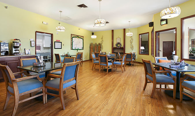 A well-lit dining room with wooden flooring, featuring tables and chairs arranged neatly.
