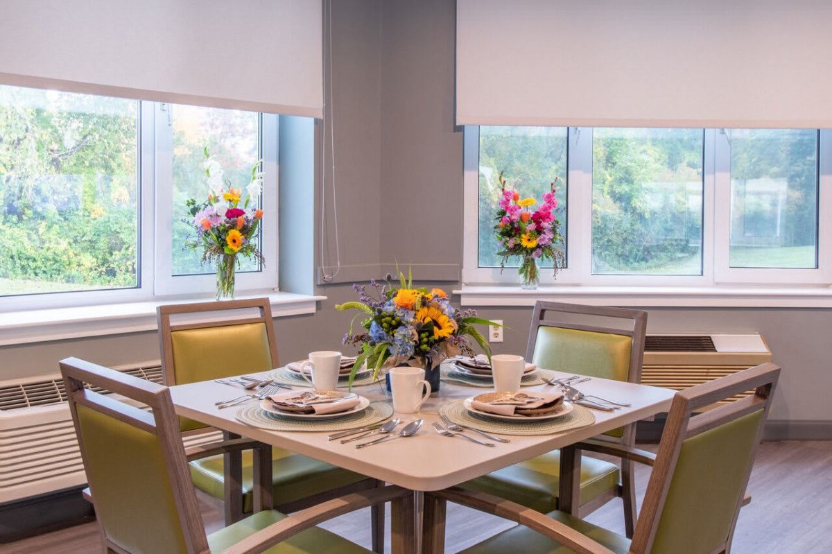 A beautifully set dining table with vibrant floral arrangements near large windows.