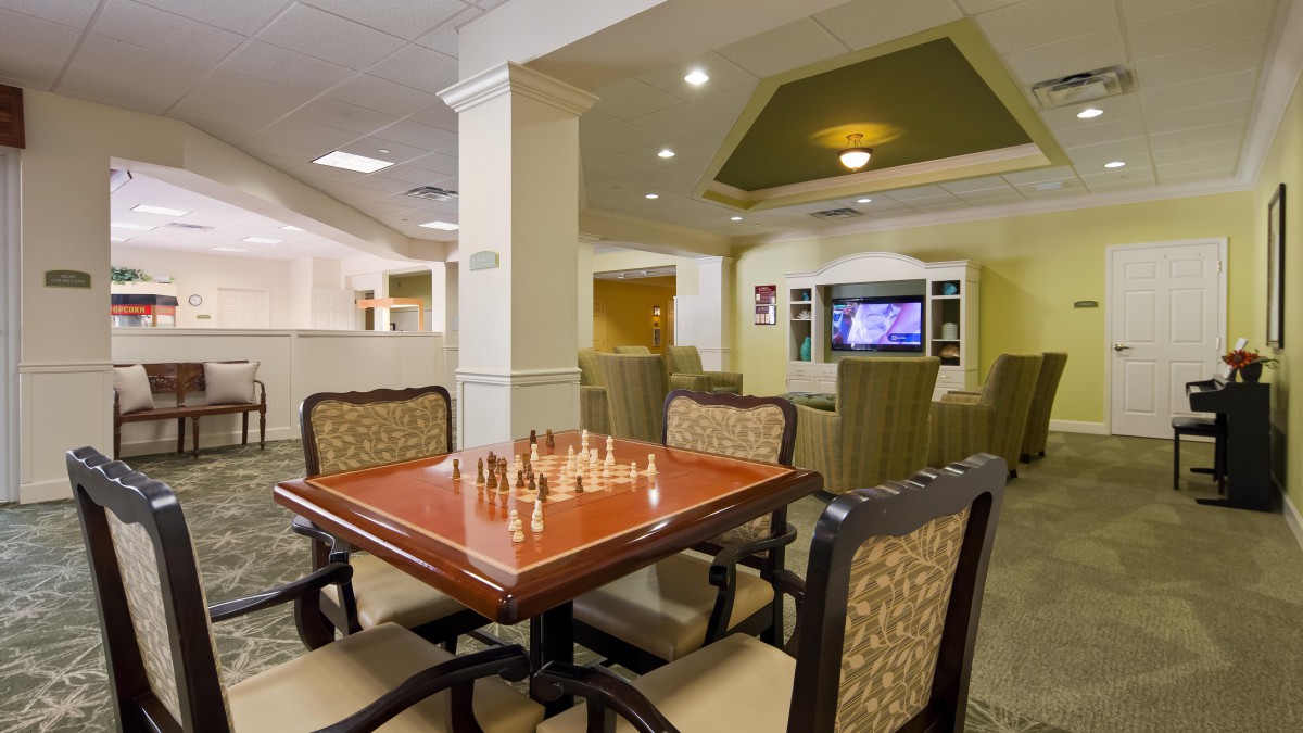 A cozy game room with a chess table and comfortable seating, featuring a TV in the background.