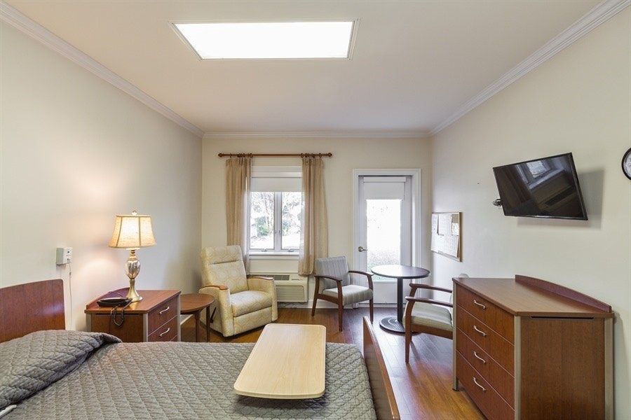 A cozy bedroom with a television, comfortable seating, and natural light from a window.