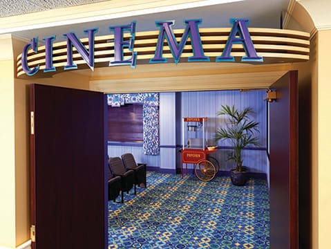 Entrance to a cinema with seating and a popcorn machine along the carpeted hallway.