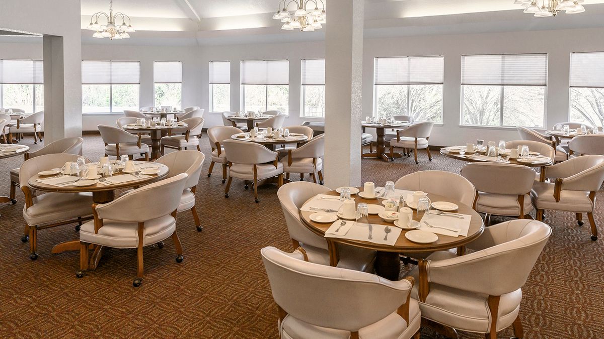 A spacious, elegantly designed dining room with neatly arranged tables and chairs, featuring large windows that allow natural light to brighten the space.