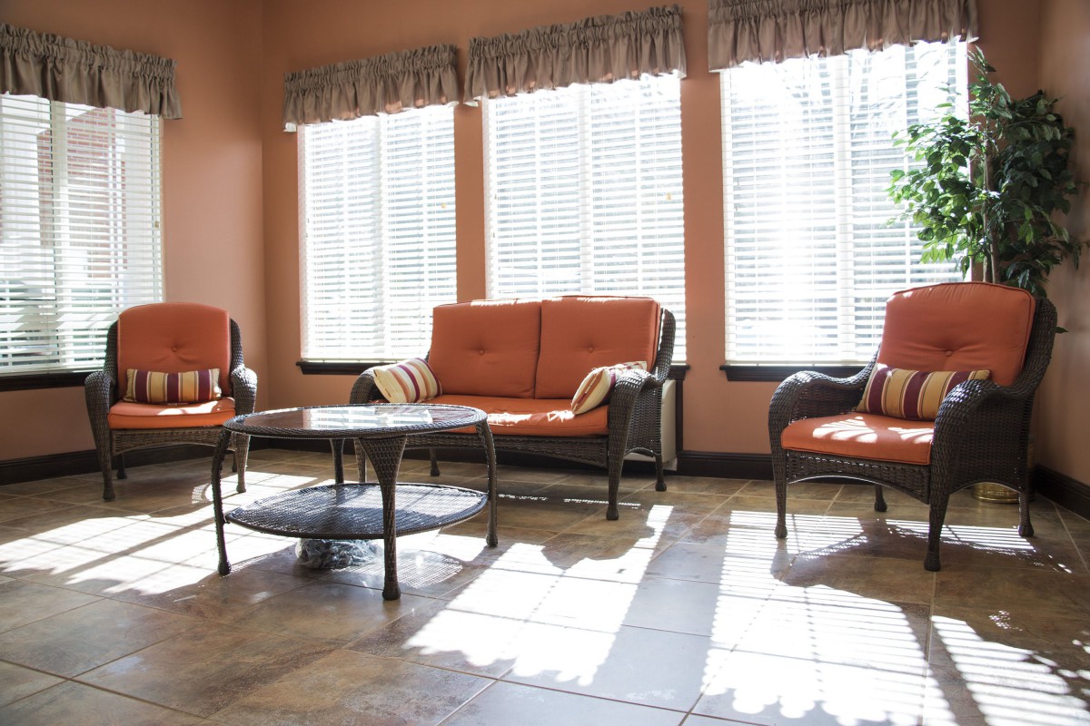 A bright living room with orange cushioned furniture and large windows letting in natural light.
