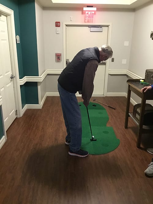 A man practicing putting indoors on a green mat.