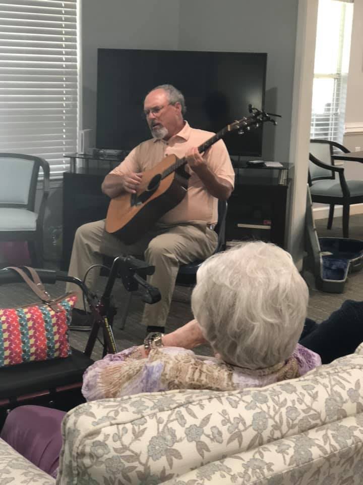 A man playing guitar in front of a small audience in an indoor setting.