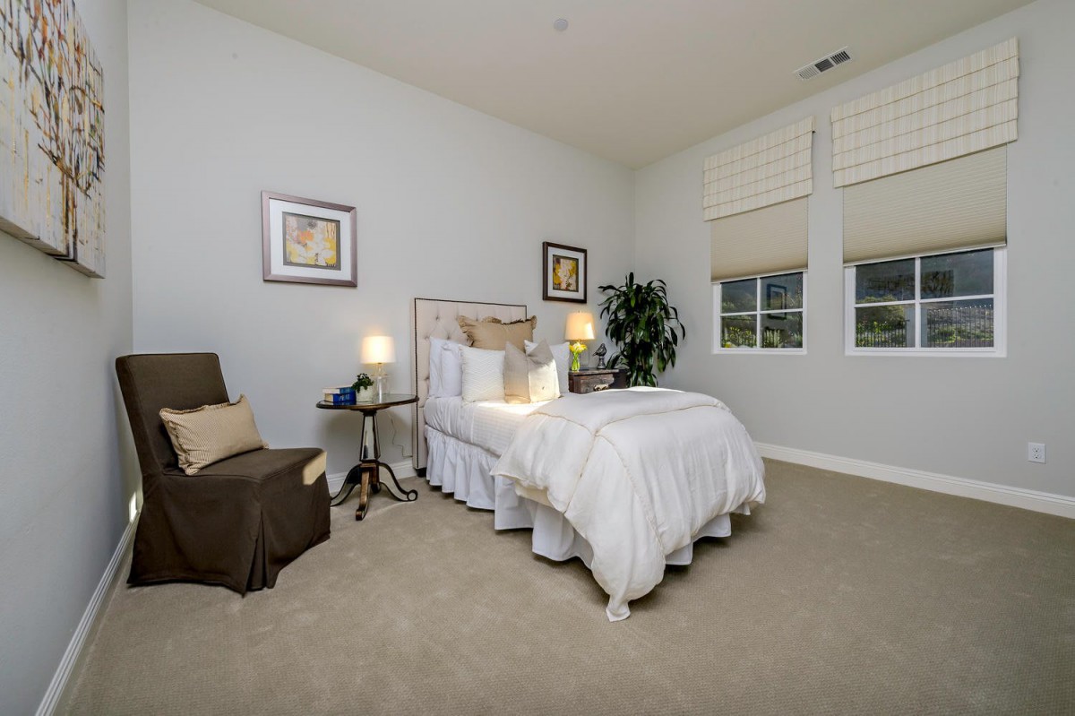 A cozy bedroom with a neatly made bed, comfortable chair, and warm lighting.