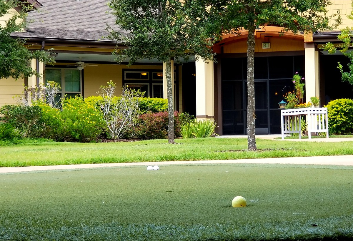 A well-maintained lawn with a yellow ball in front of a building surrounded by trees and shrubs.