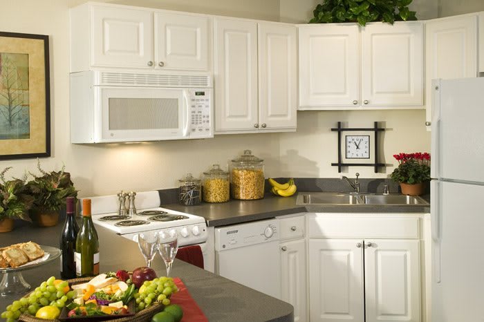 A cozy kitchen with white cabinets, featuring a microwave, countertops adorned with decor and fruit.