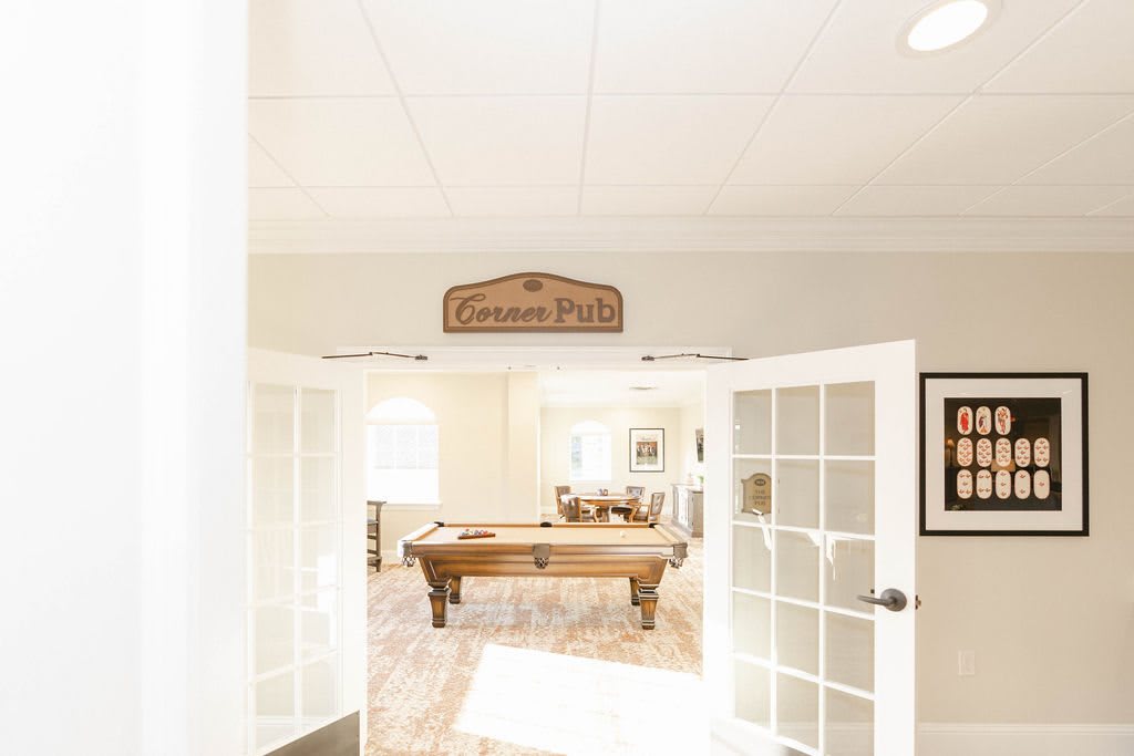 A bright game room with a pool table, viewed through glass double doors.