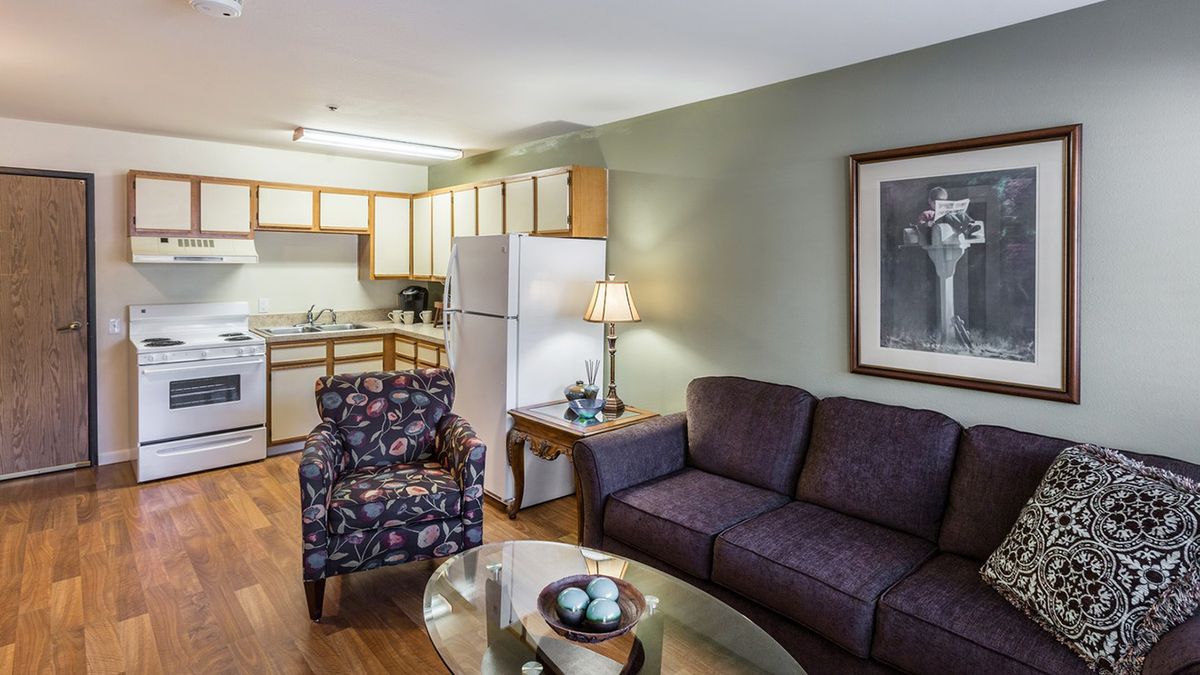 A cozy living room with a view of the kitchen, featuring a sofa, armchair, and modern decor.