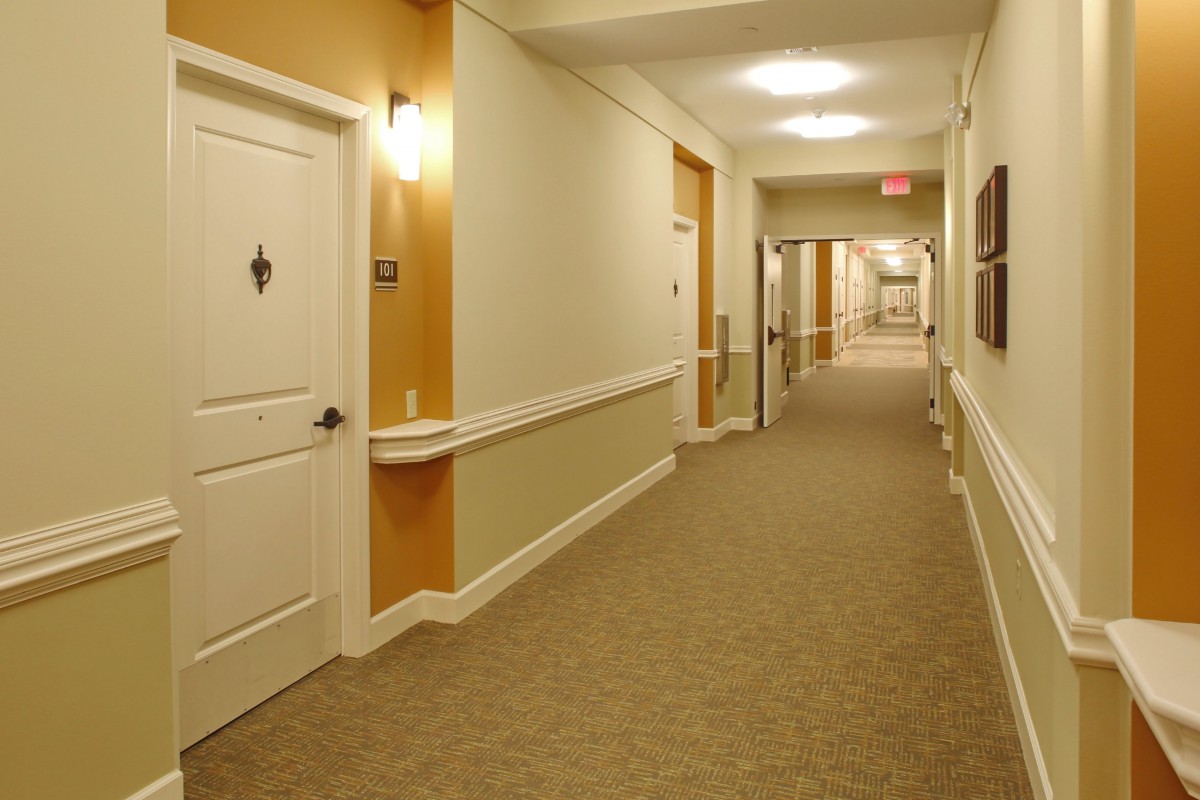 A long hallway in a building with multiple doors and carpeted flooring.