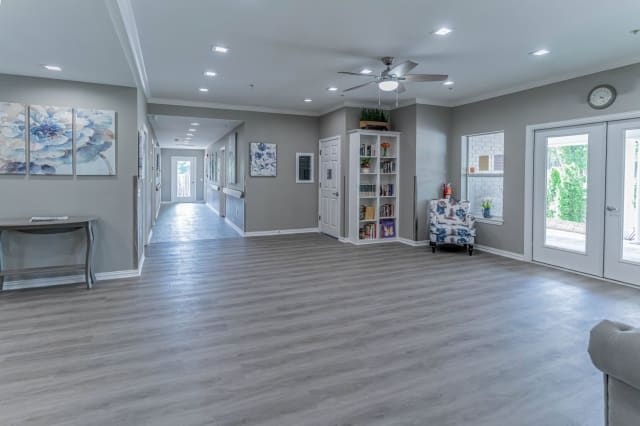 A spacious living area with modern wood flooring, large windows, and a ceiling fan provides a comfortable and stylish space.
