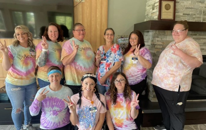 A group of people wearing tie-dye shirts posing indoors with peace signs.