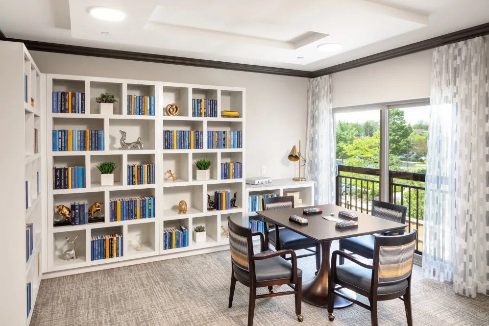 A cozy reading area with a bookshelf, table, and chairs next to a window.