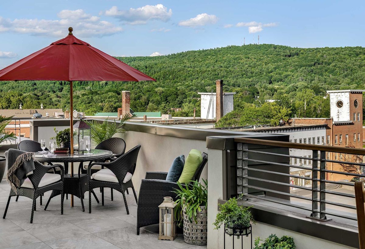 A peaceful patio with outdoor furniture and a red umbrella overlooks lush green hills.