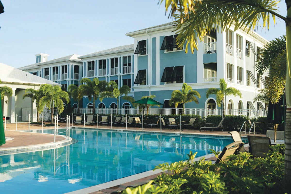 A tropical resort featuring a large swimming pool surrounded by palm trees and a multi-story building.