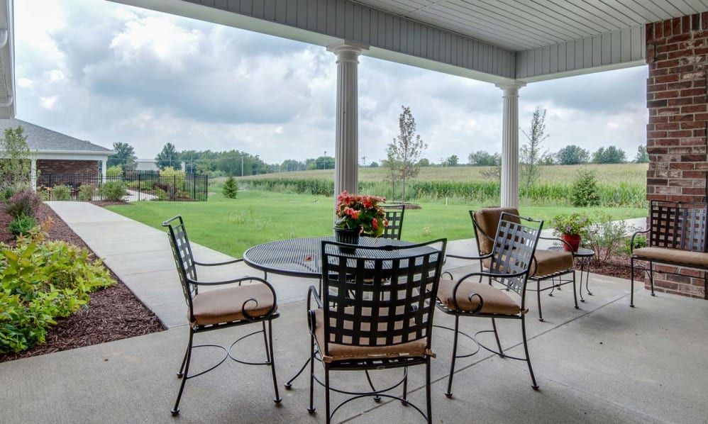 A covered patio with metal chairs and a table overlooking a green landscape.