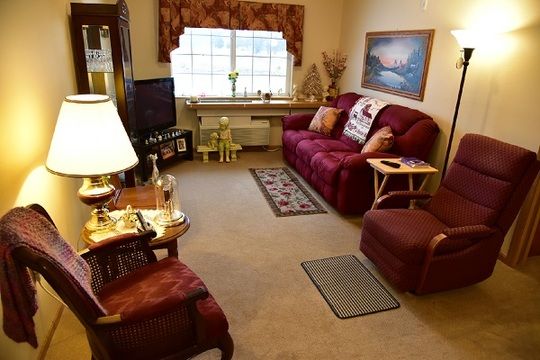 A cozy living room with a maroon sofa, armchair, and a small television.