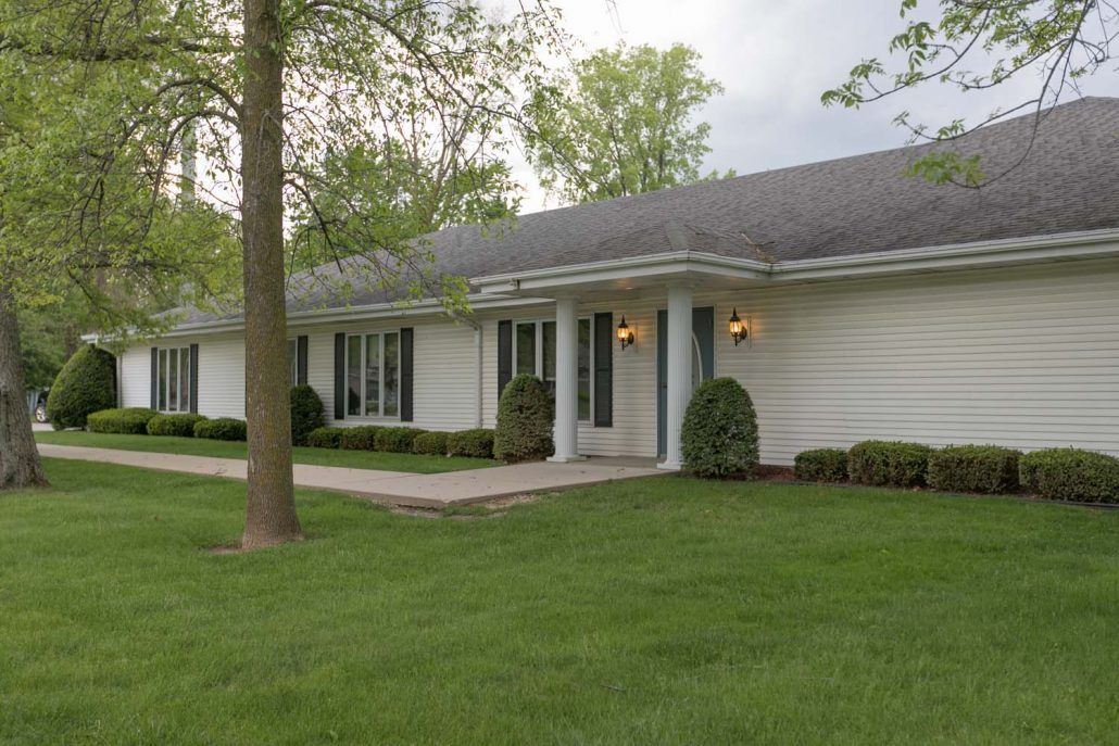 A single-story residential house with a well-maintained lawn and surrounding trees.