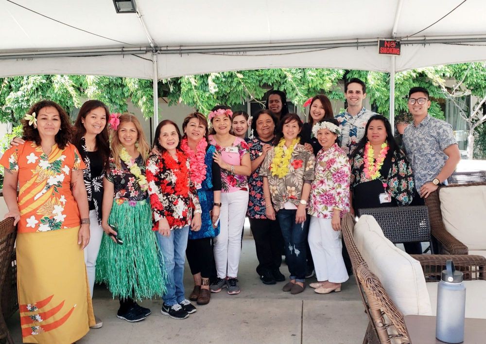 A group of people posing together at an outdoor event with a Hawaiian theme, wearing colorful leis and floral prints.