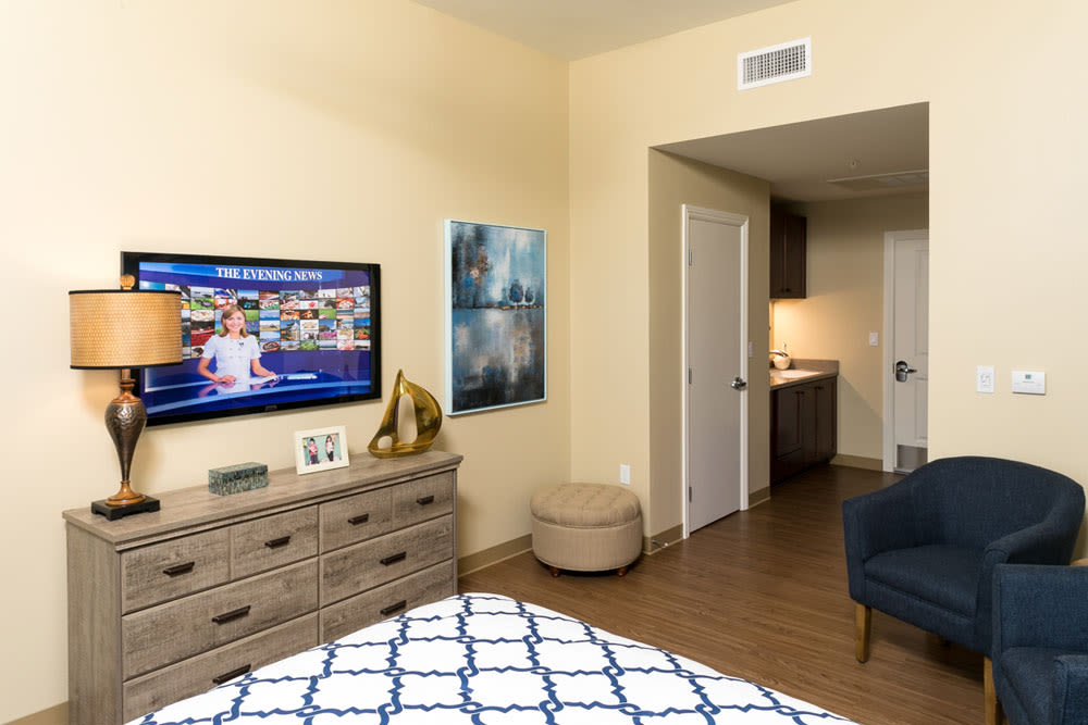 A modern bedroom with a TV mounted on the wall, a dresser with decor items, and a cozy bed.