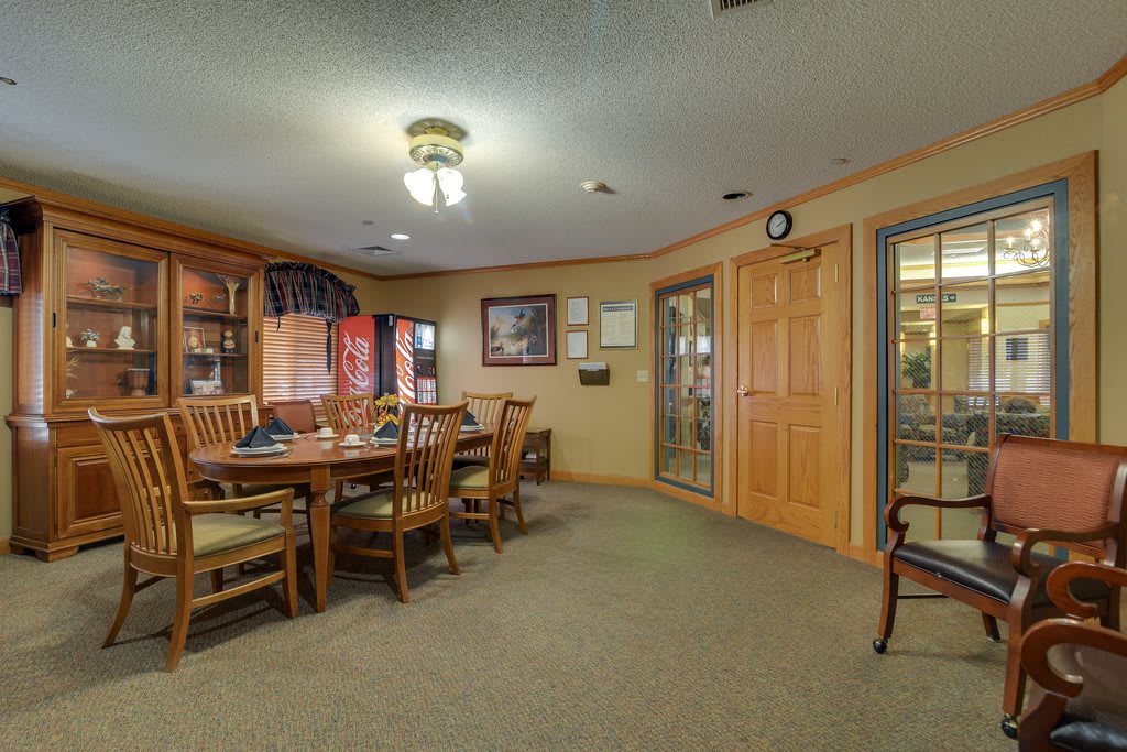 A cozy dining room with wooden furniture and bookshelves, illuminated by ceiling lights.