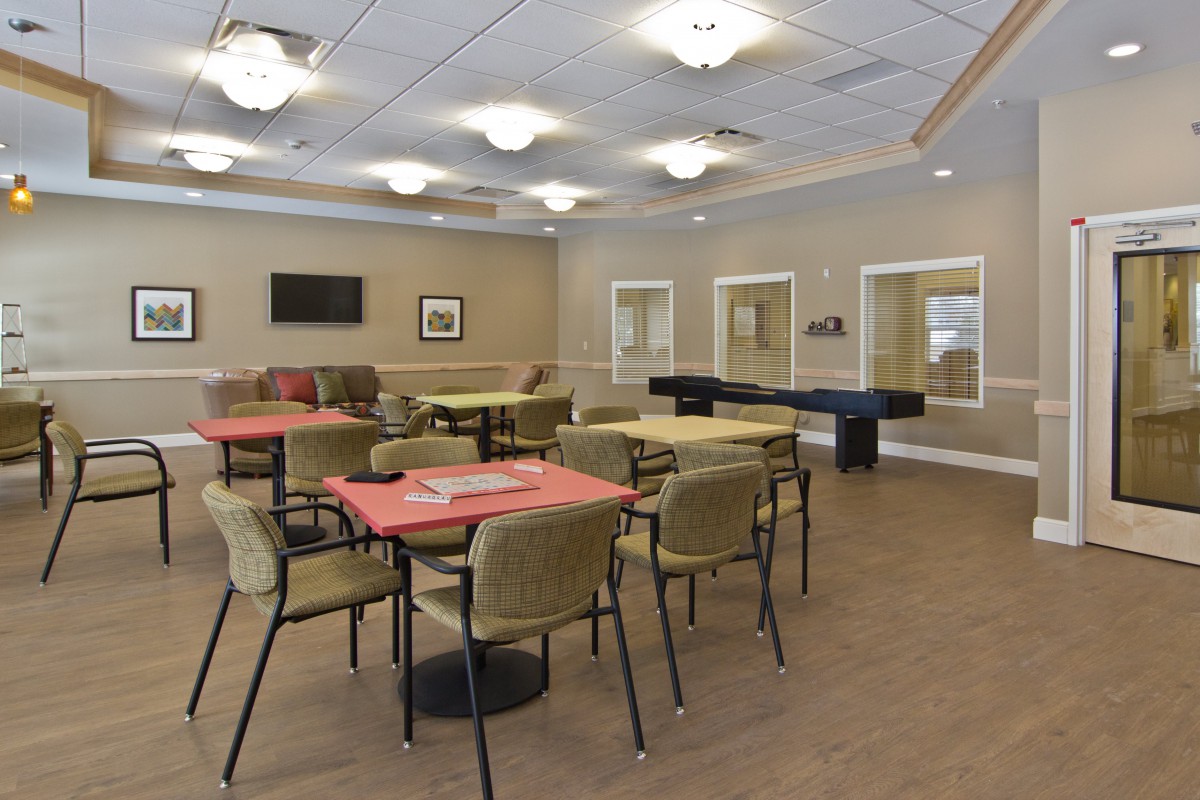 A spacious community room with modern furnishings, featuring tables, chairs, and a recreational area.