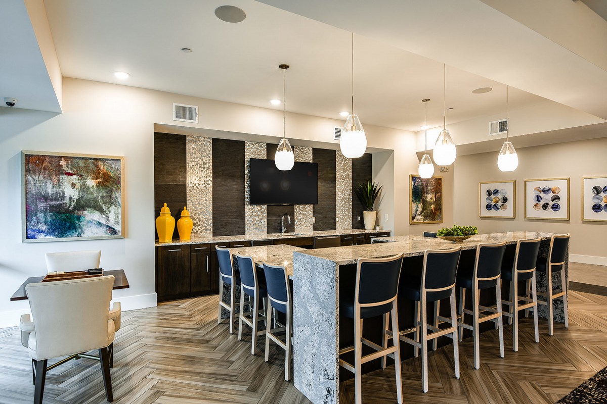 A modern kitchen with a large island, surrounded by bar stools and illuminated by pendant lights.