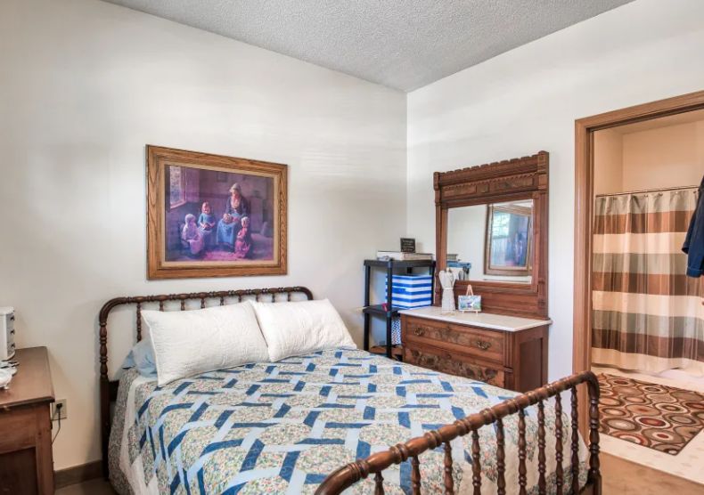 A cozy bedroom with vintage decor, featuring a quilt-covered bed and a wooden dresser with a mirror.