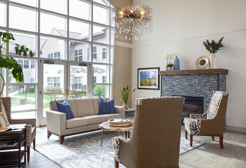 A modern living room with a large window, stylish sofa, chairs, and fireplace.