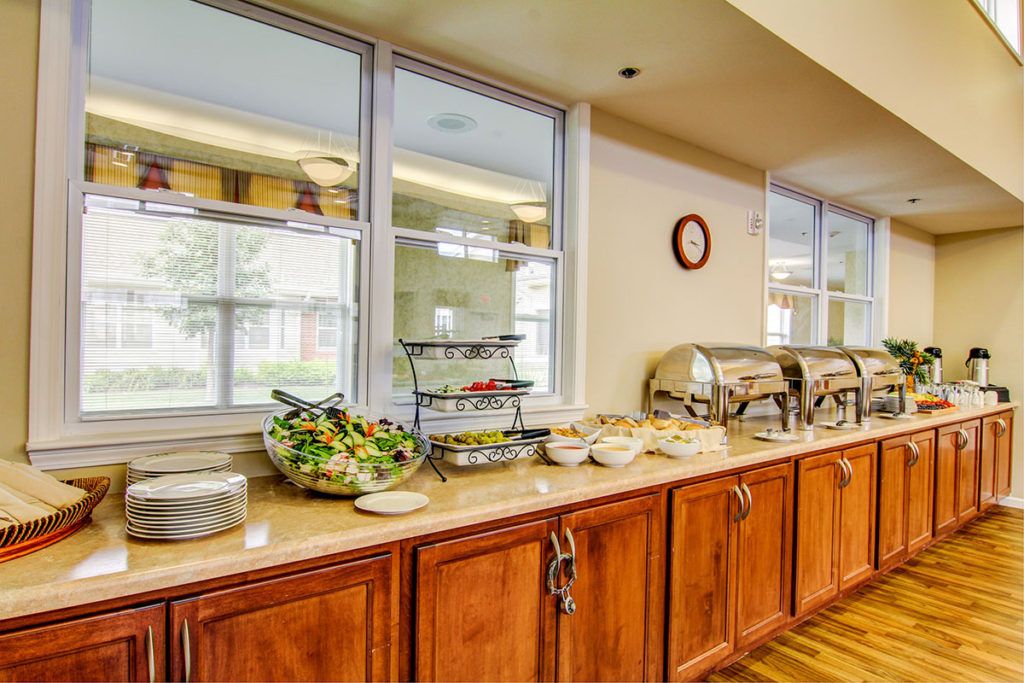 A self-service buffet setup with chafing dishes and a salad bowl on a wooden counter.