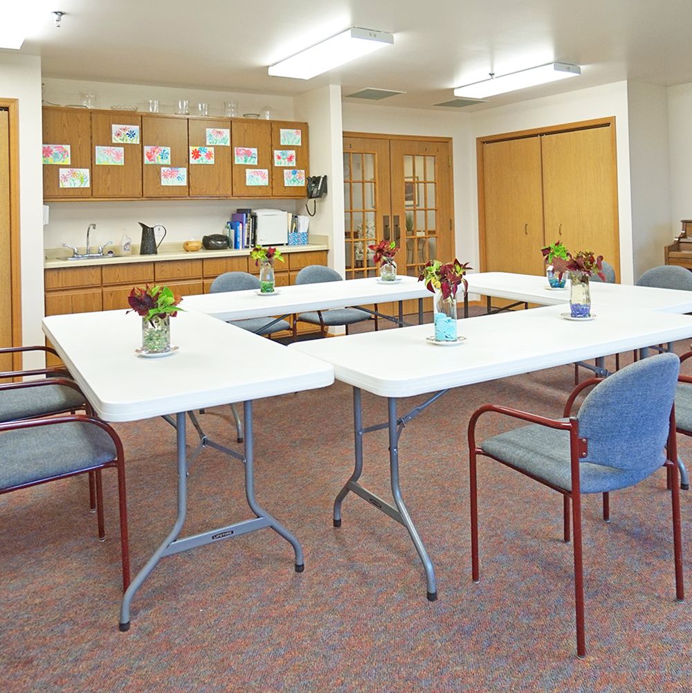 A brightly lit community center meeting room with arranged tables and chairs.