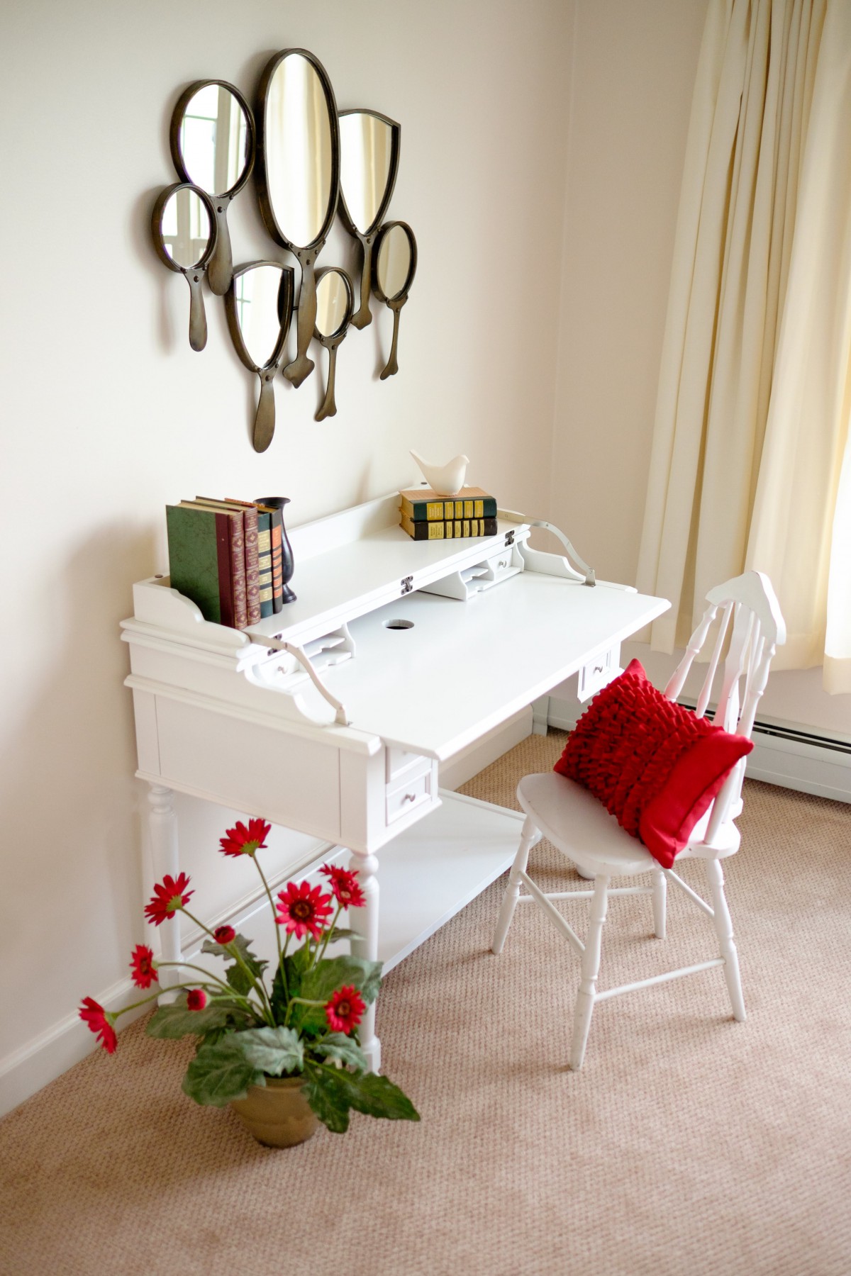 A cozy home office with a white desk and chair, adorned with red accents and mirror wall decor.