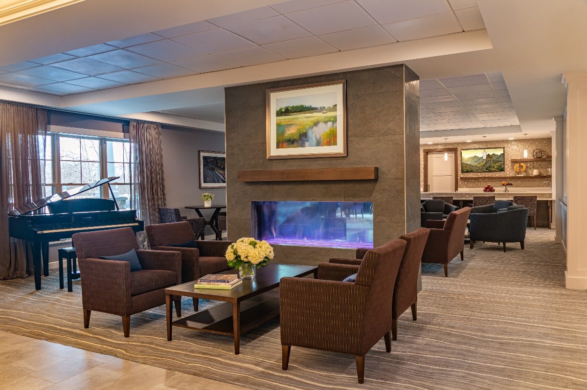 A cozy hotel lobby with modern decor, featuring a seating area around a central fireplace and elegant furnishings.