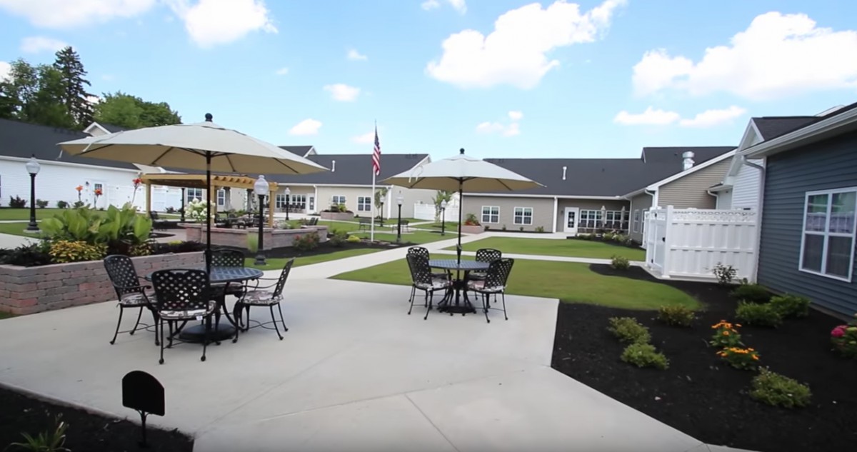 A spacious outdoor patio area with tables and umbrellas set against a backdrop of well-maintained landscaping and buildings.