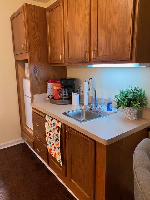 A small kitchen area featuring a sink, wooden cabinets, and various appliances.