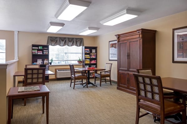 A cozy room with tables and chairs, surrounded by bookshelves and illuminated by overhead lighting.