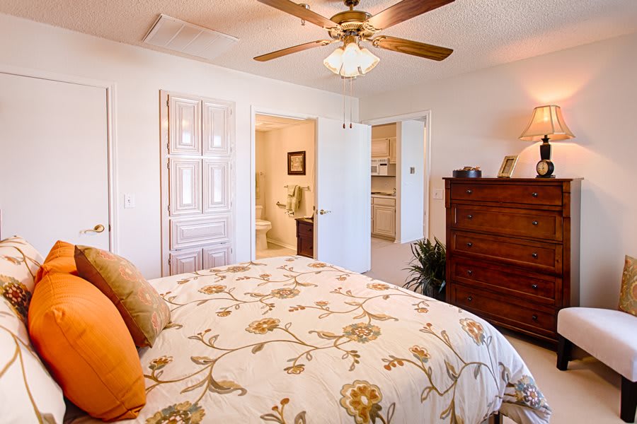 A cozy bedroom with a floral-themed double bed, ceiling fan, and wooden dresser.