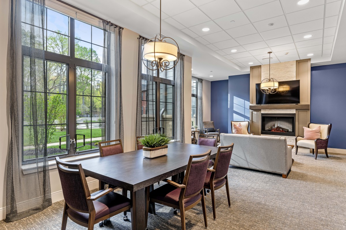 A modern dining and living area with large windows, elegant furniture, and a cozy fireplace.