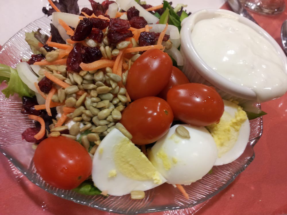 A fresh salad with cherry tomatoes, boiled eggs, seeds, shredded carrots, and a bowl of dressing.